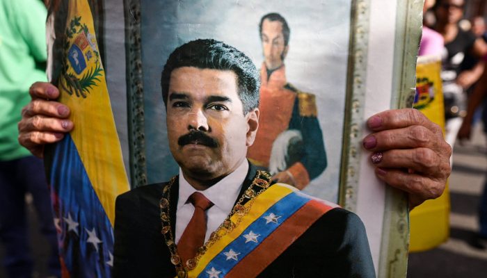 Uma pessoa segura a imagem do presidente venezuelano Nicolás Maduro enquanto apoiadores do governo se reúnem após um ataque dos EUA à Venezuela, neste sábado (3)
             -       
        Gaby Oraa/REUTERS